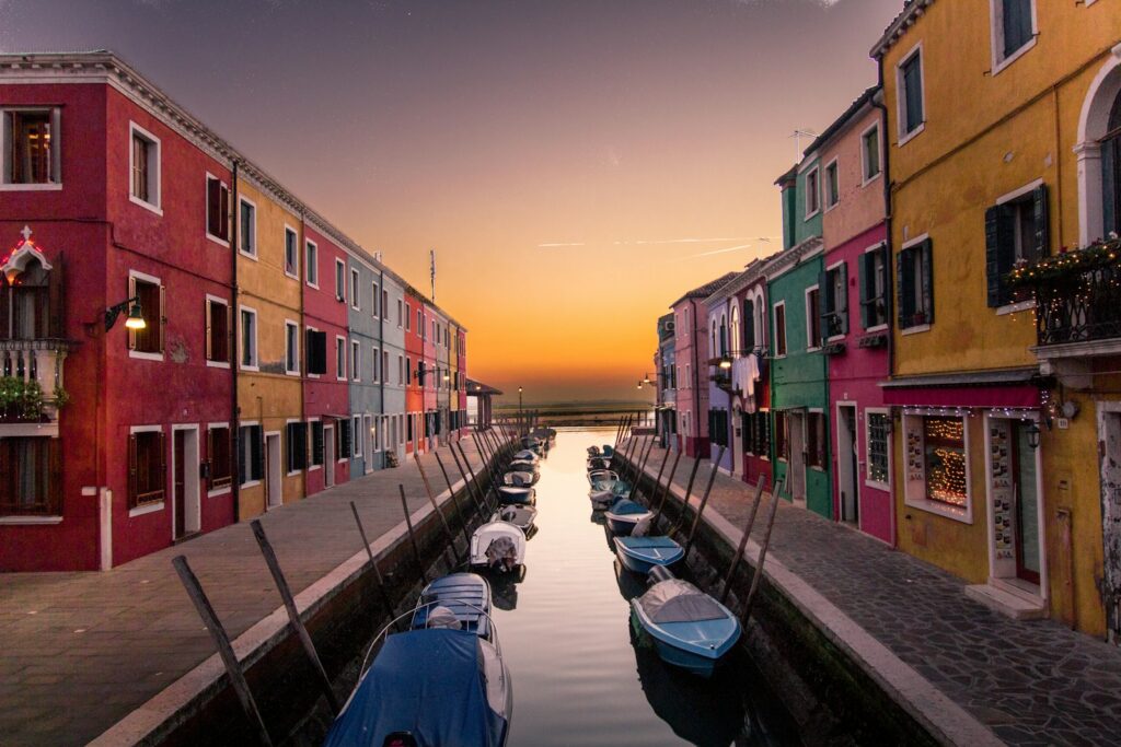 barcos azuis estacionados no rio entre edifícios multicoloridos ao pôr do sol em Veneza