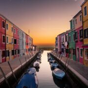 blue boats parked on river between multicolored buildings at sunset venice