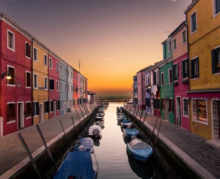 blue boats parked on river between multicolored buildings at sunset venice