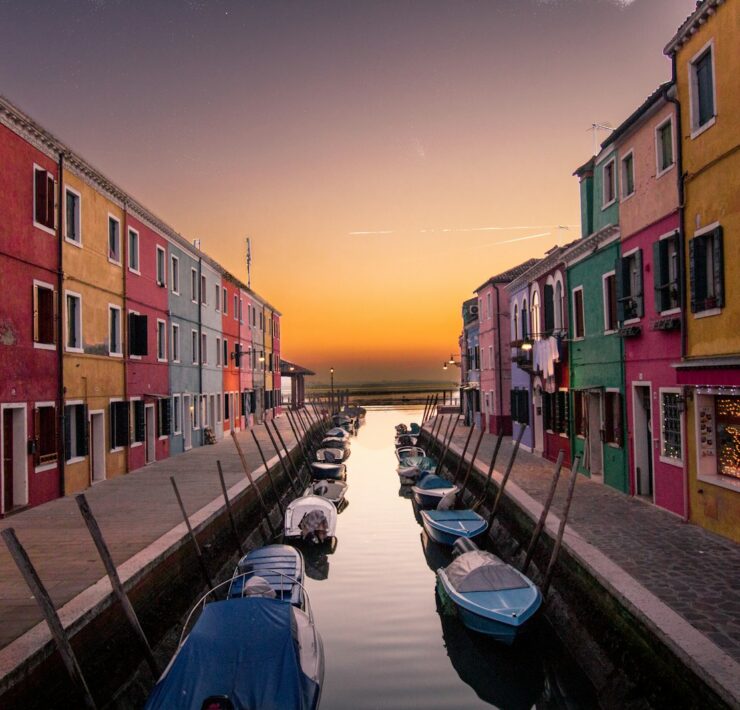 blue boats parked on river between multicolored buildings at sunset venice