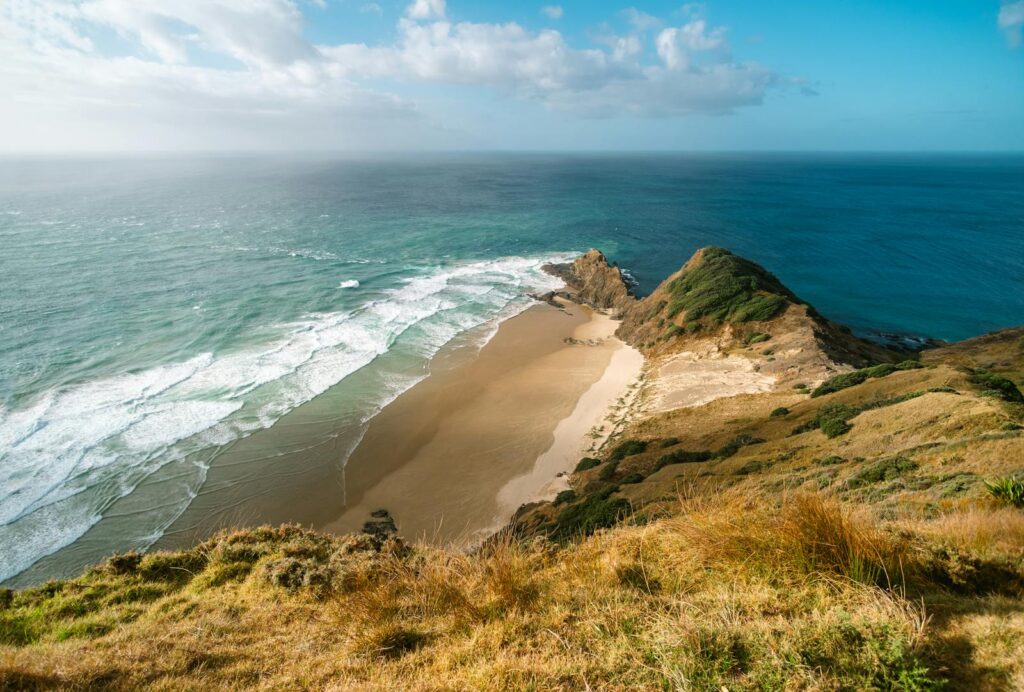 Vista aérea deslumbrante do litoral de Cape Reinga, na Nova Zelândia, exibindo praias douradas e o Oceano Pacífico.