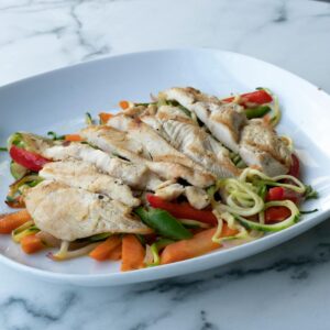 Healthy grilled chicken breast served on zucchini noodles and fresh vegetables.