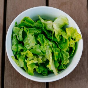 Crisp green lettuce in a white bowl on a rustic wooden surface. Perfect for healthy eating.