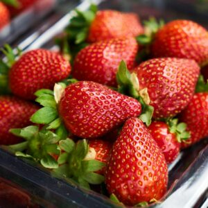 Close-up of ripe strawberries in a clear plastic container, showcasing vibrant freshness and juicy appeal.