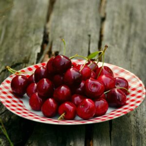 A vibrant display of red cherries on a patterned plate outdoors, perfect for summer themes.