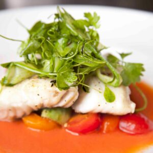 A beautifully presented gourmet fish dish topped with fresh herbs and vibrant vegetables.