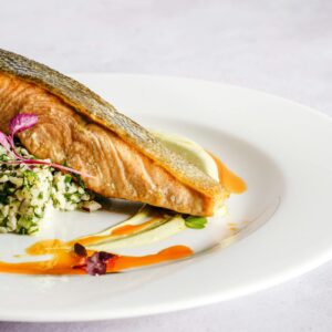 A beautifully plated salmon dish with quinoa, herbs, and a vibrant sauce, perfect for gourmet food lovers.