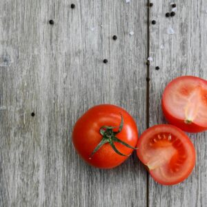 Close-up of ripe tomatoes on a rustic wooden table with peppercorns.