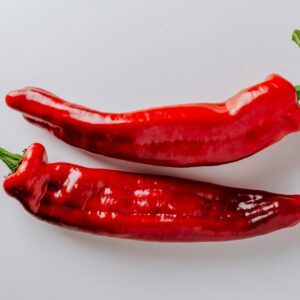 From above of pair of hot chili peppers with green sprouts and smooth surface put on white table