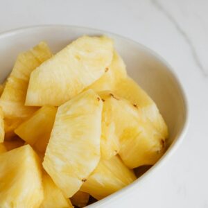 From above of fresh pieces of ripe pineapple served in white deep plate and placed on marble table