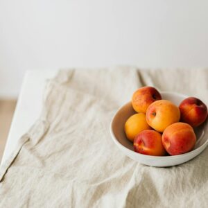 Bunch of ripe apricots in bowl placed on creasy tablecloth on white table