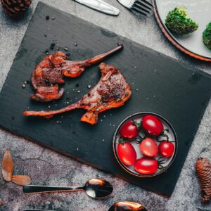 Delicious lamb chops served with cherry tomatoes on a slate board, perfect for a gourmet meal.