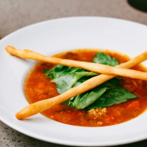Delicious tomato soup garnished with spinach and breadsticks in a white bowl.