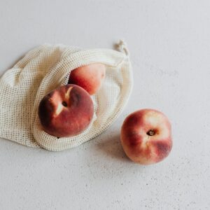 Three fresh peaches in a sustainable net bag on a white background, promoting zero waste.