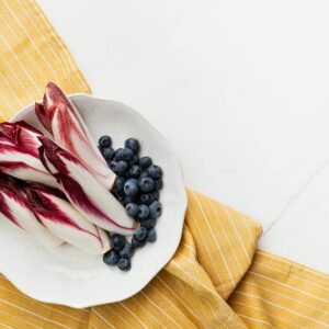 A top view of Belgian endive and blueberries on a plate placed on a yellow striped cloth.