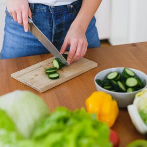 Healthy food preparation with fresh cucumbers and vegetables on a wooden table.