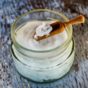 Close-up of organic coconut oil in glass jar with wooden spoon, perfect for natural health and wellness use.