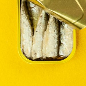 Top view of an open tin of sardines on a vibrant yellow background, showcasing seafood in oil.