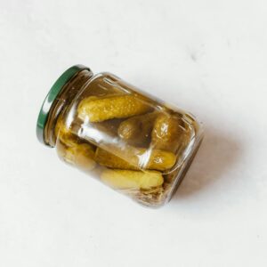 Glass jar with pickled cucumbers on a white surface, showcasing classic still life photography.