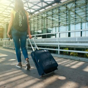 Uma mulher caminha com uma mala do lado de fora de um terminal de aeroporto, pronta para viajar.