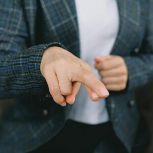 Crop anonymous female in classy outfit showing crossed fingers to camera while sitting in armchair and communicating with hand language