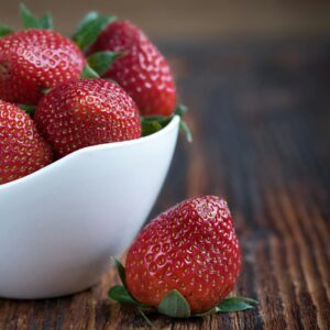 Close-up of fresh strawberries in a white bowl on a rustic wooden table, highlighting vibrant red color.