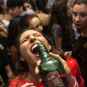 Exciting party scene with young adults enjoying drinks and dancing under colorful lights.