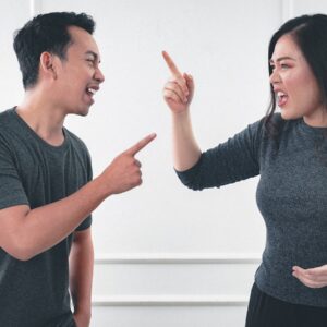 um homem e uma mulher com roupas escuras discutem colocando o dedo no rosto do outro