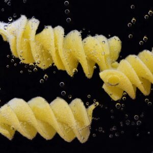 três pedaços de macarrão fusilli mergulhados na água