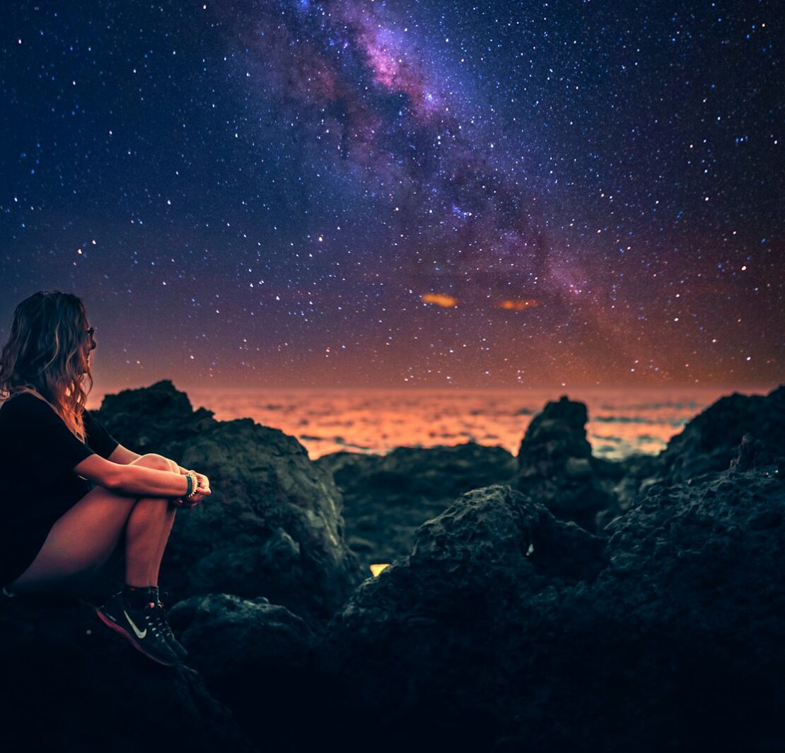 mulher sentada em uma pedra durante a noite com a via lactea ao fundo