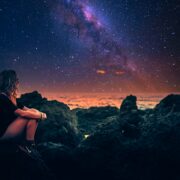 mulher sentada em uma pedra durante a noite com a via lactea ao fundo