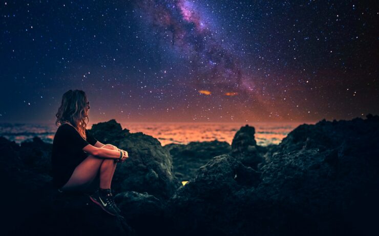mulher sentada em uma pedra durante a noite com a via lactea ao fundo