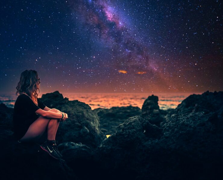 mulher sentada em uma pedra durante a noite com a via lactea ao fundo