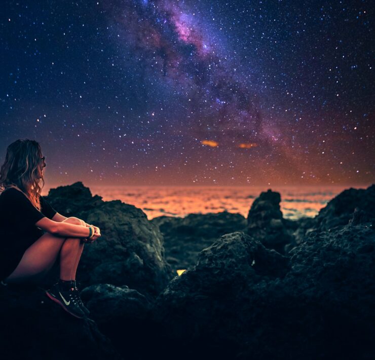 mulher sentada em uma pedra durante a noite com a via lactea ao fundo