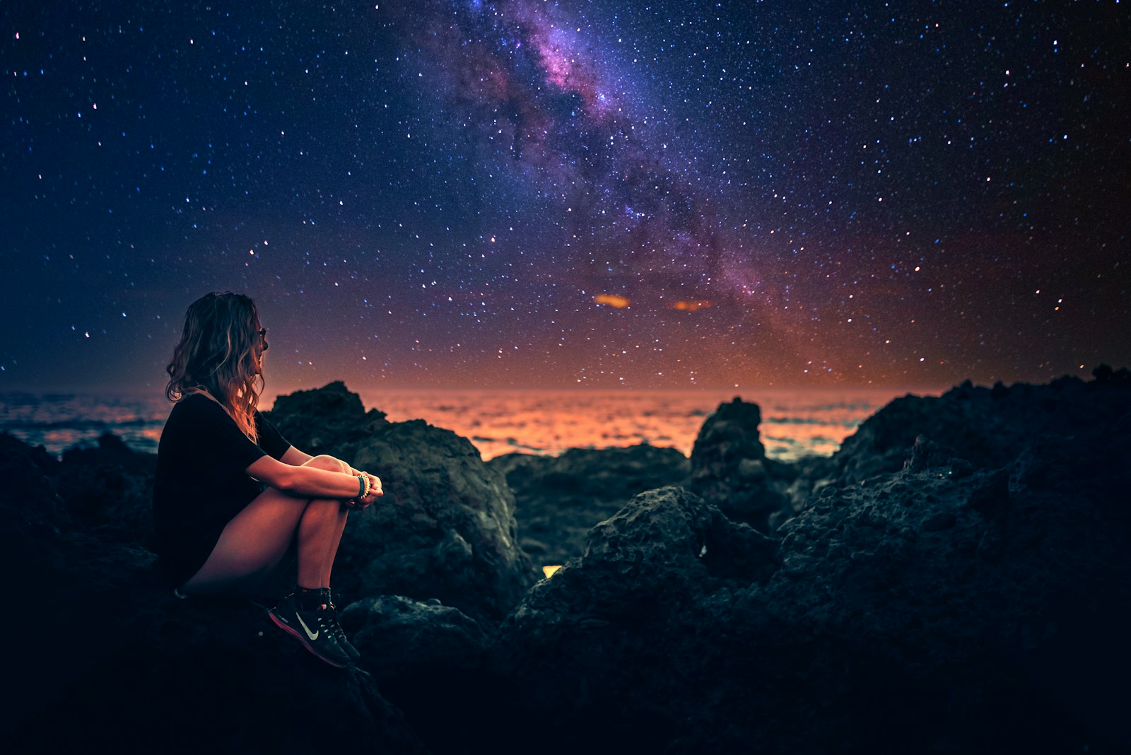 mulher sentada em uma pedra durante a noite com a via lactea ao fundo