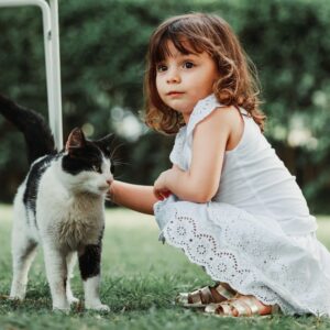 uma menina ajoelhada ao lado de um gato preto e branco