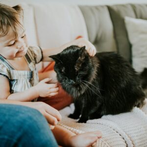 menina sentada no sofá ao lado de um gato preto