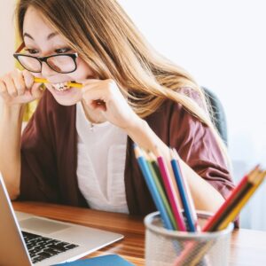 Mulher mordendo um lápis enquanto está sentada em uma cadeira em frente ao computador durante o dia.
