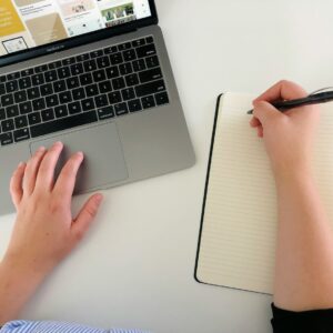 pessoa usando um laptop e escrevendo em um caderno ao mesmo tempo