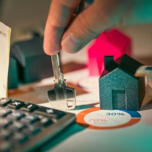 pessoa segurando uma chave ao lado de um computador com miniaturas de casas e outras coisas