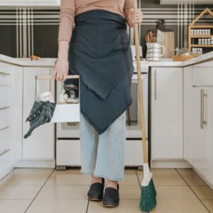 uma mulher parada na cozinha segurando uma vassoura