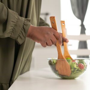 pessoa mexendo a salada com utensílios enormes