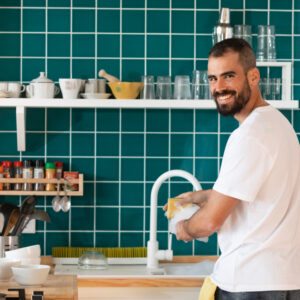 homem sorrindo e lavando a louça da cozinha