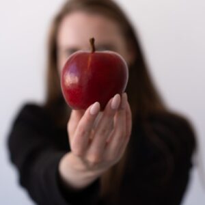 A woman in black offers a red apple, symbolizing temptation and health.
