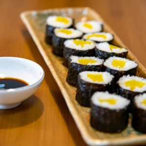 prato retangular com diversos tipo de sushi e uma vasilha de molho de soja ao lado
