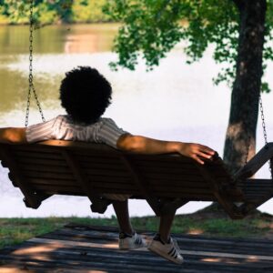 person sitting on hammock facing lake