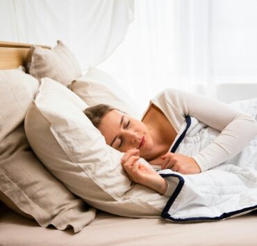uma mulher dormindo em uma cama com um edredom branco
